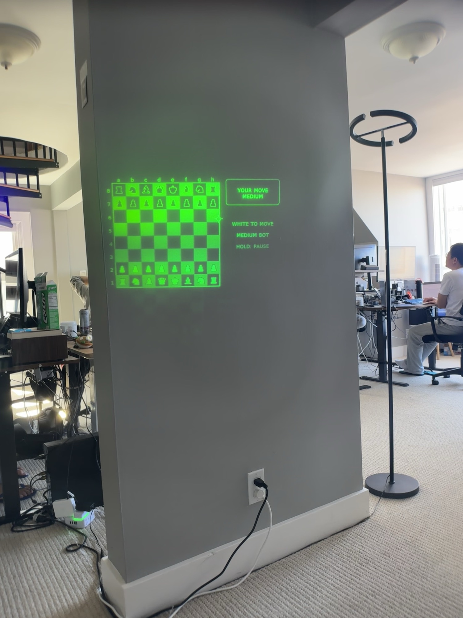 A chess board projected in green onto a wall, mid-game against a bot
